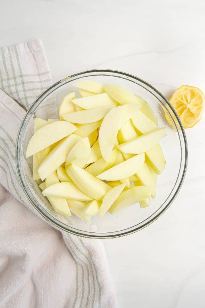 Sliced apples in clear bowl mixed with lemon juice.