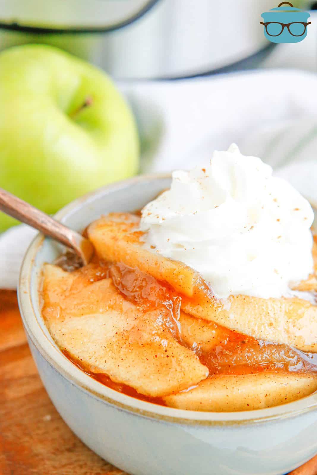 Side view of Instant Pot Fried Apples in bowl with whipped cream and spoon.