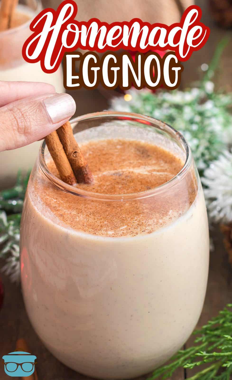 Pinterest image of hand putting cinnamon stick into glass of Homemade Eggnog.