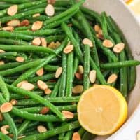 Square image of Almond Green Beans in bowl with half a lemon.