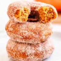 Square image of stacked Pumpkin Donuts with top one broken in half.