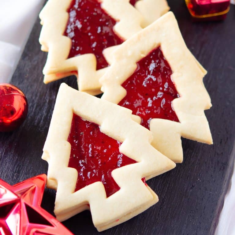 Square image of Christmas Tree Linzer cookies on black platter.