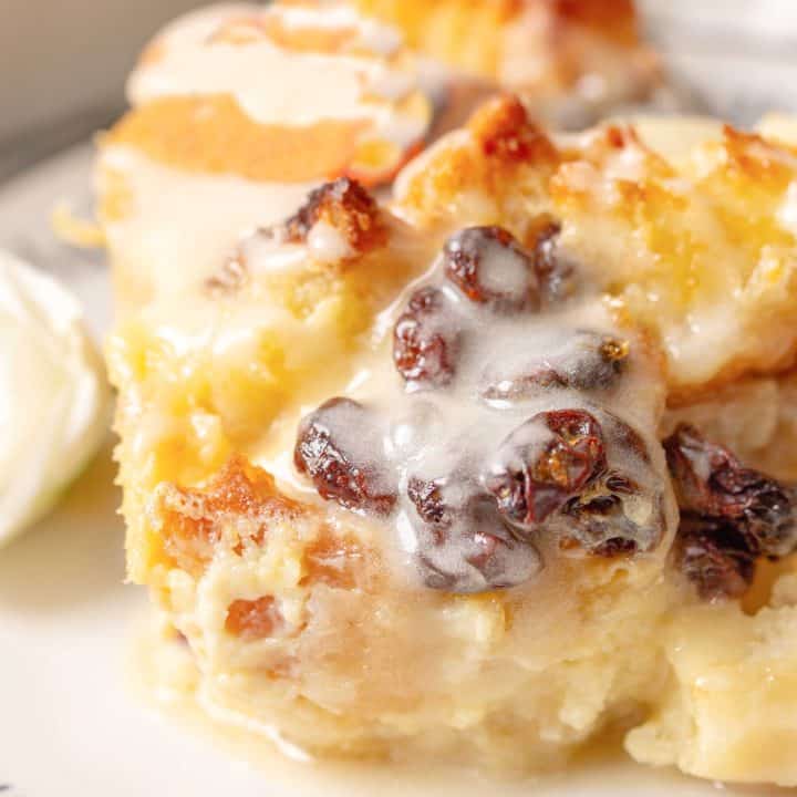 Square image of Old Fashioned Bread Pudding slice with sauce and raisins.