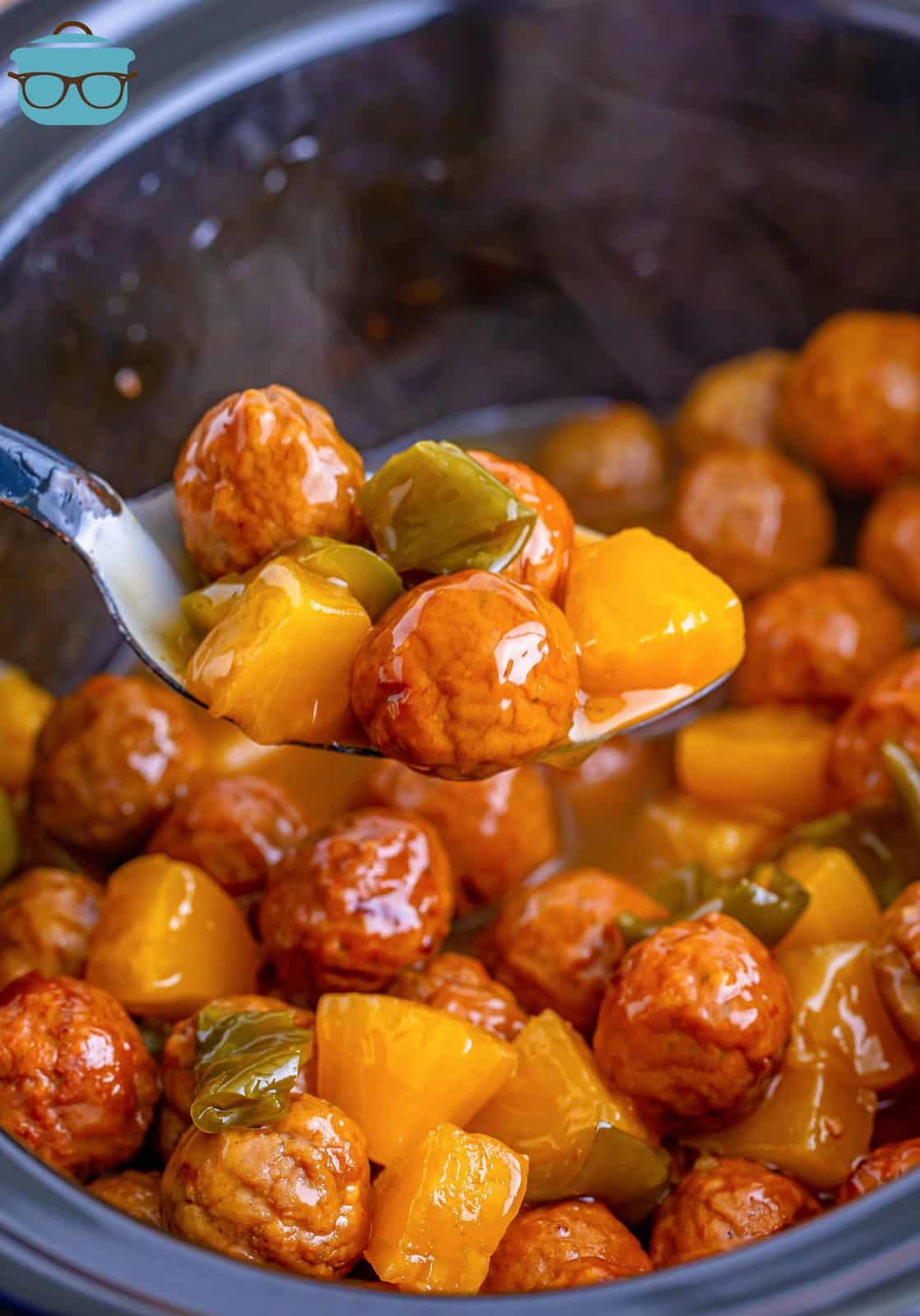 a silver spoon holding up some sweet and sour meatballs over the crock pot.