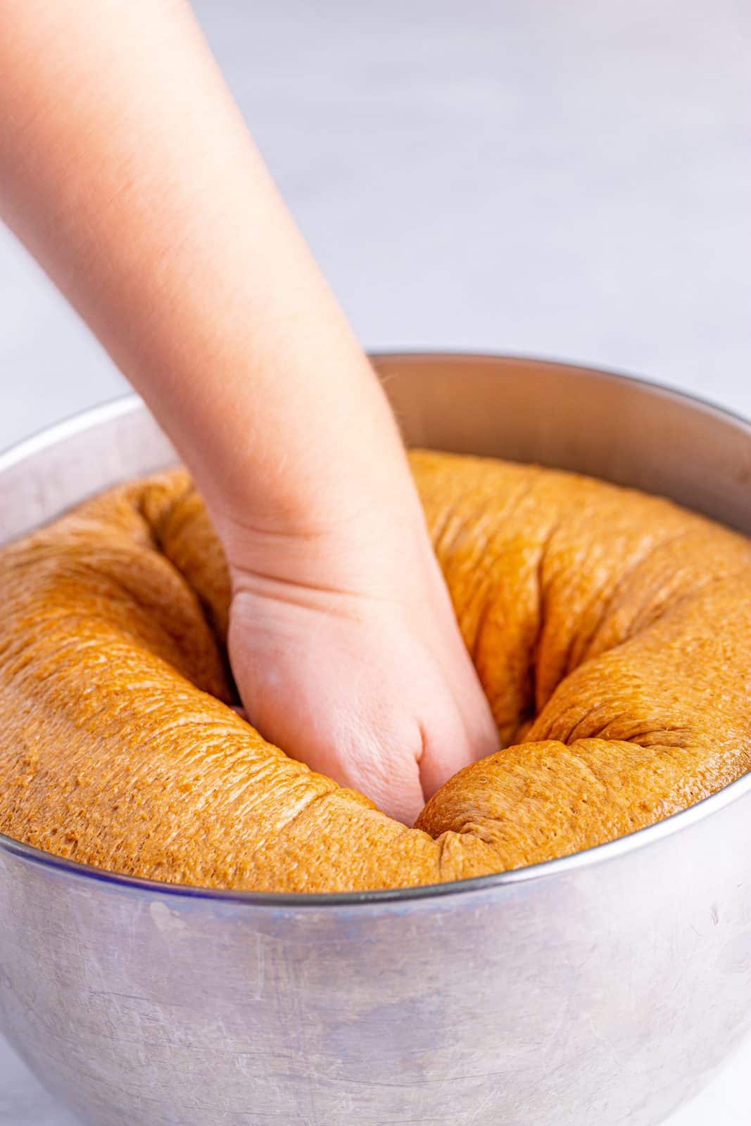 Hand punching risen bread dough down.