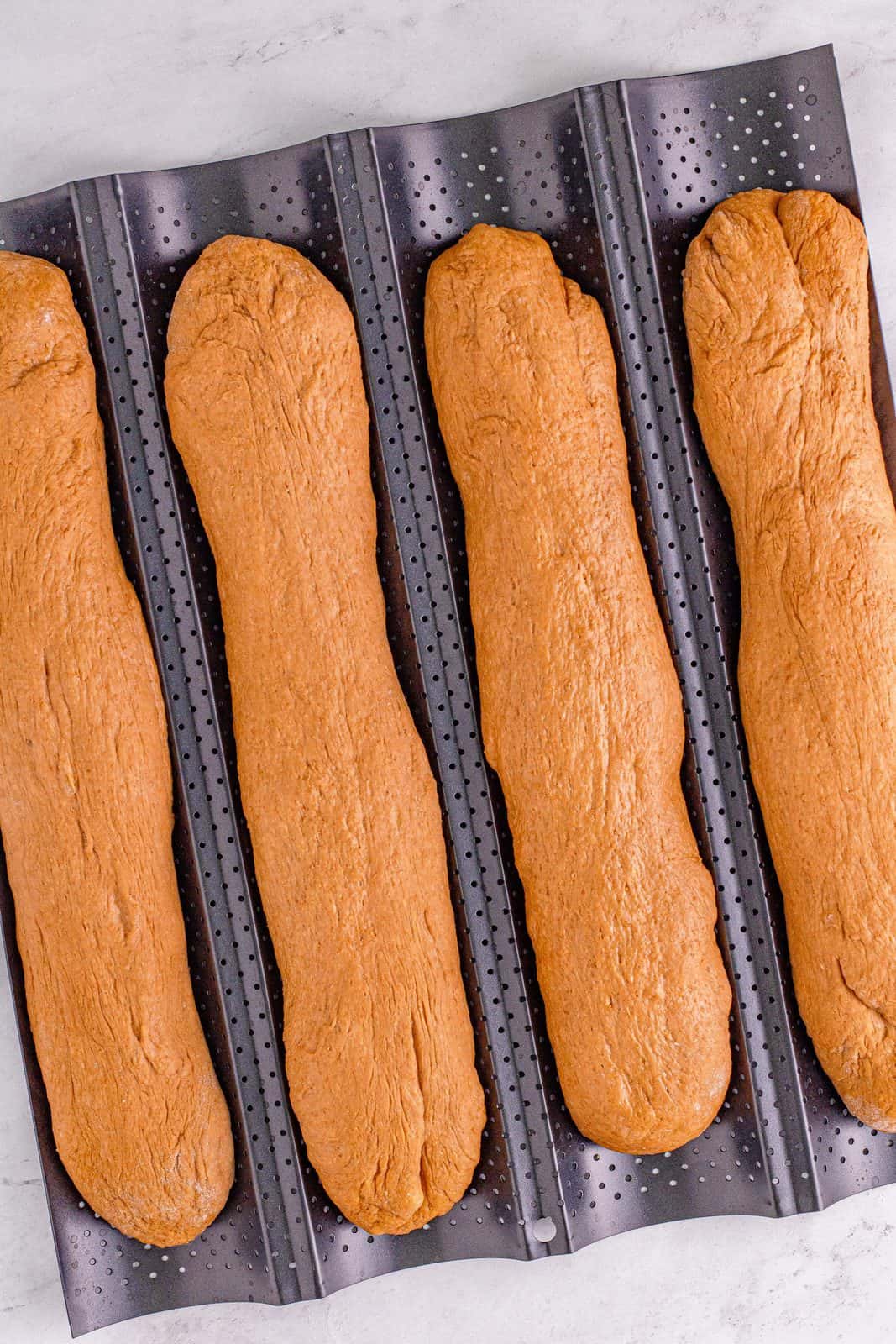 Logs of bread dough placed on a baguette pan.