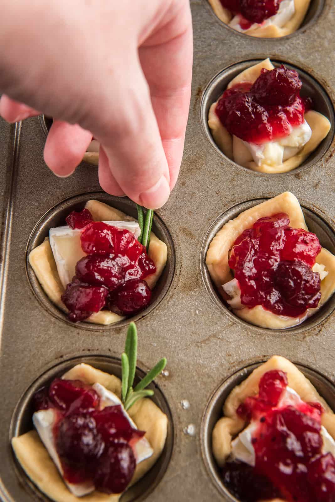 a hand adding a small rosemary leaf to cranberry brie bite.