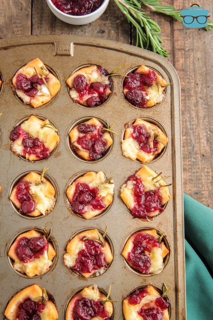 overhead photo of cranberry brie appetizers in a muffin tin on a wood surface.