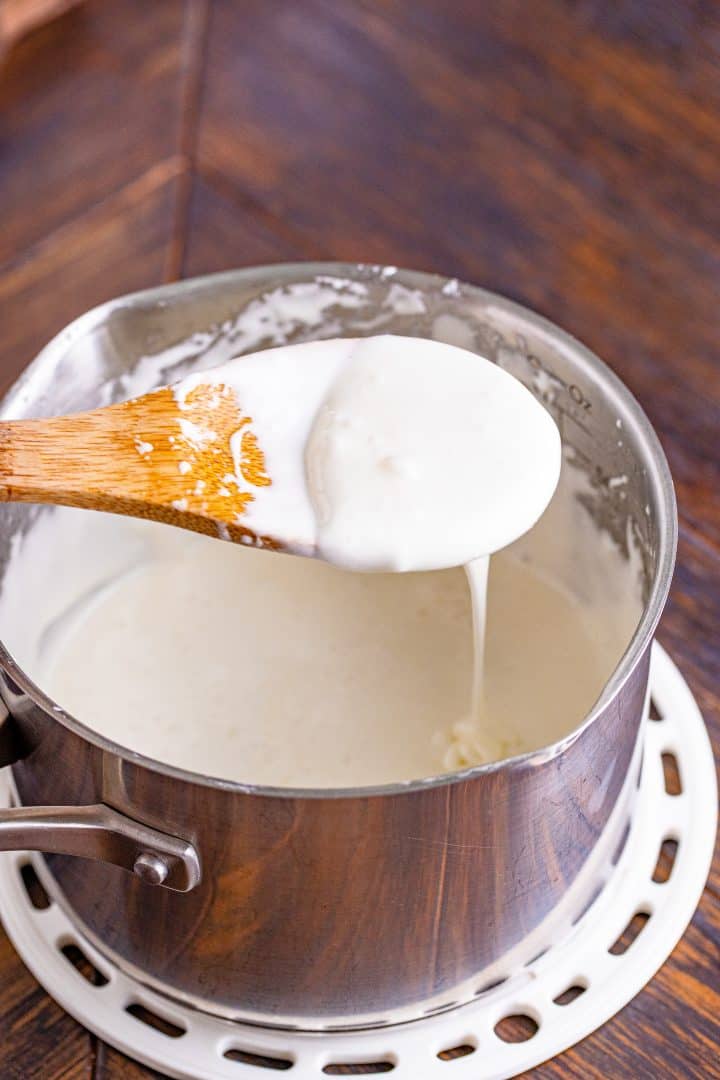 melted marshmallow mixture being held up with a wooden spoon over a sauce pan.