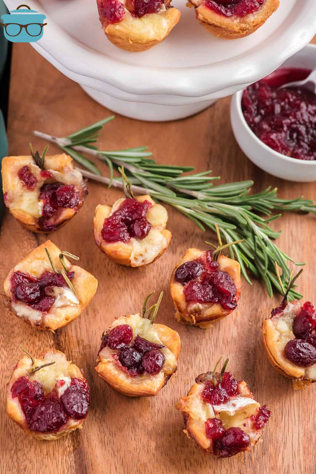 several cranberry brie bites on a wooden surface with a white cake pedestal in the background.