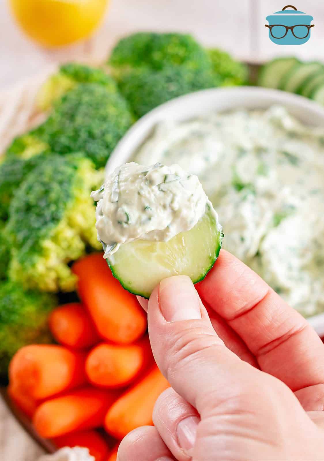 Hand holding up a cucumber with dip on it.