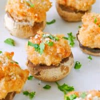 Square image of Crab Cake Stuffed Mushrooms topped with parsley on white plate.