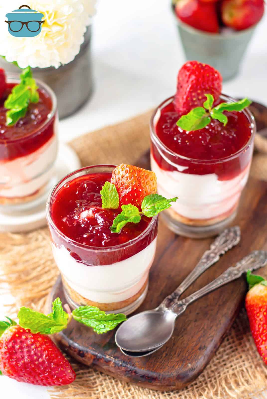 Overhead photos of two Strawberry Cheesecake Parfaits in glasses topped with strawberries and mint.