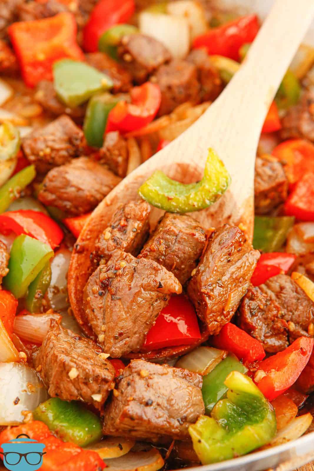 Steak Tips with Peppers on wooden spoon in pan.