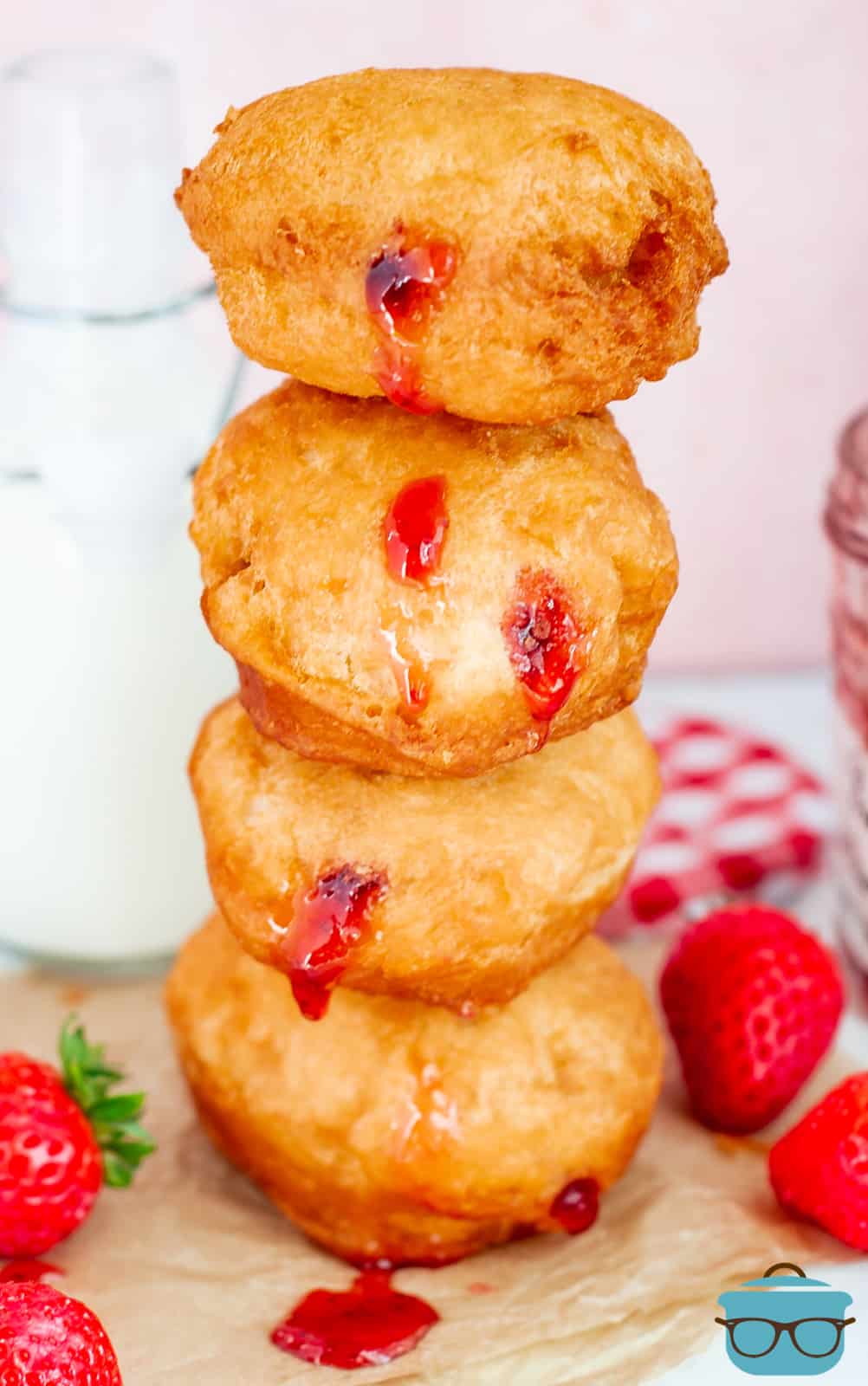 Stacked Strawberry Jelly Filled Biscuit Donuts on top of one another with strawberries surrounding them.