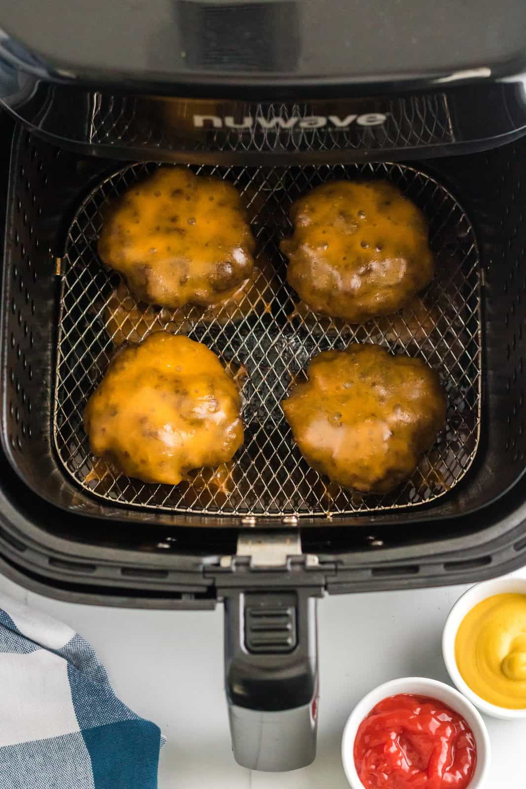 Cheese melted over Air Fryer Hamburgers in air fryer basket.