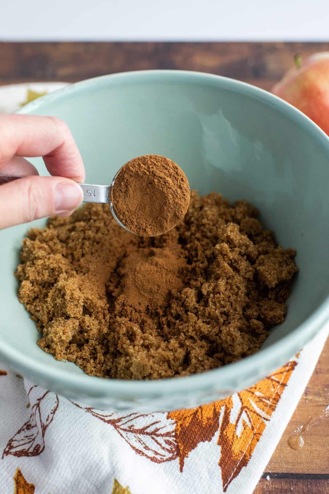 Cinnamon, brown sugar and nutmeg being mixed together in bowl.