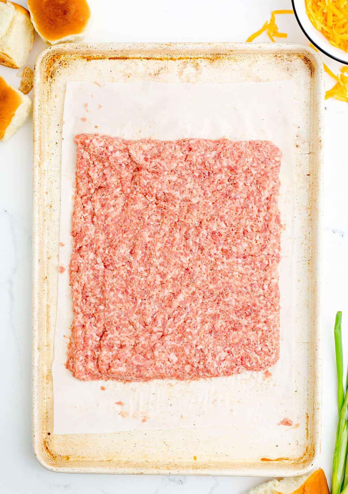 Pork sausage pressed into a rectangle on parchment lined baking sheet.