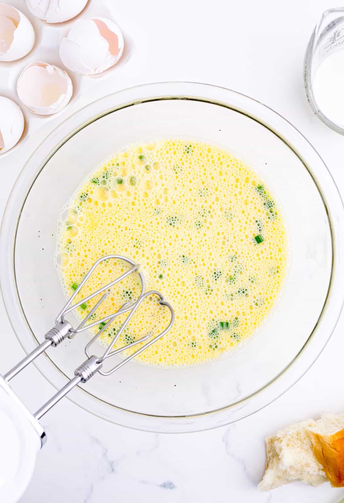 Eggs, milk, chives and pepper whisked together in bowl.