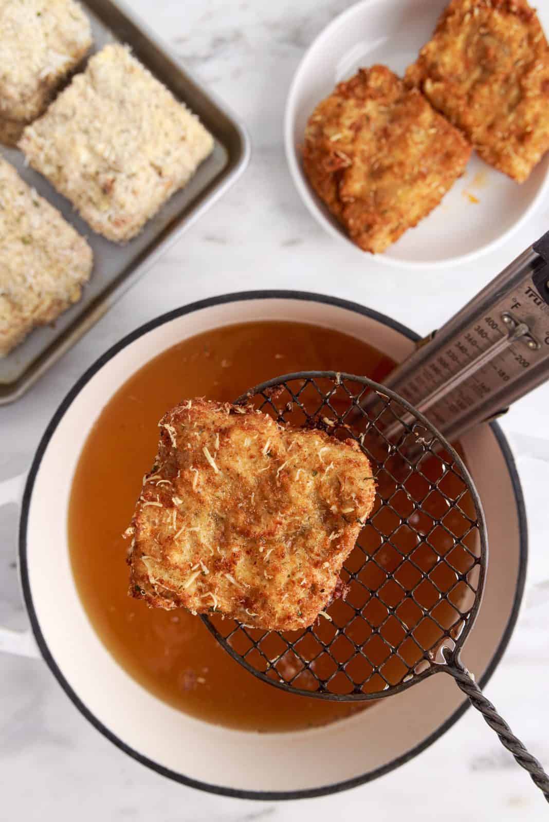 Spider strainer lifting up fried lasagna out of oil.