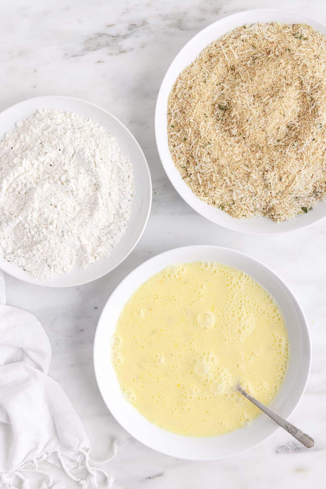 Flour, salt, and pepper combined in one dish. Milk and eggs combined together in a second dish. Breadcrumbs and cheese combined into a third dish.