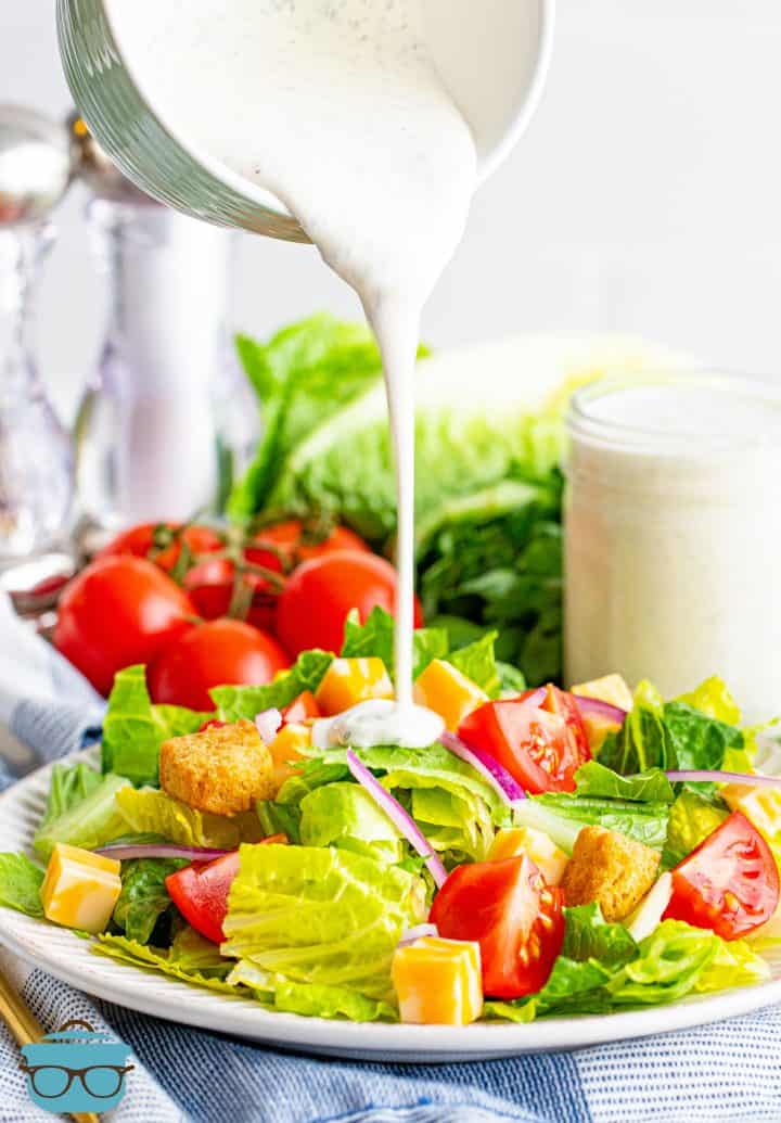 homemade ranch dressing shown being poured onto a fresh salad on a white plate. 