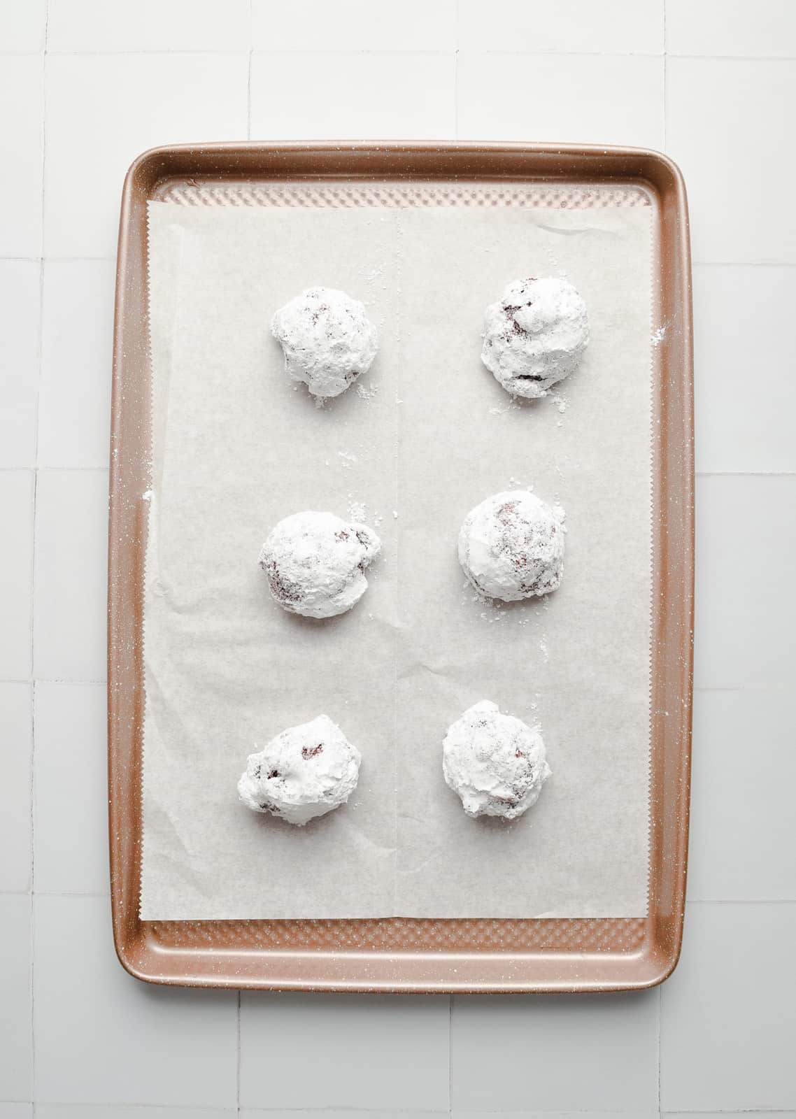 Cookie dough balls rolled in granulated and powdered sugar and placed on baking sheet.