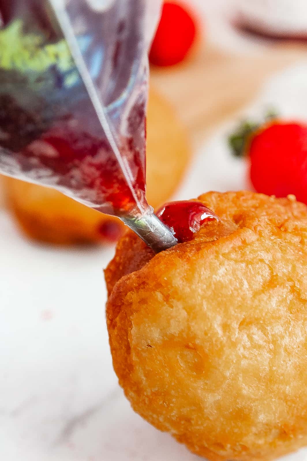 Piping bag filling donuts with jelly.