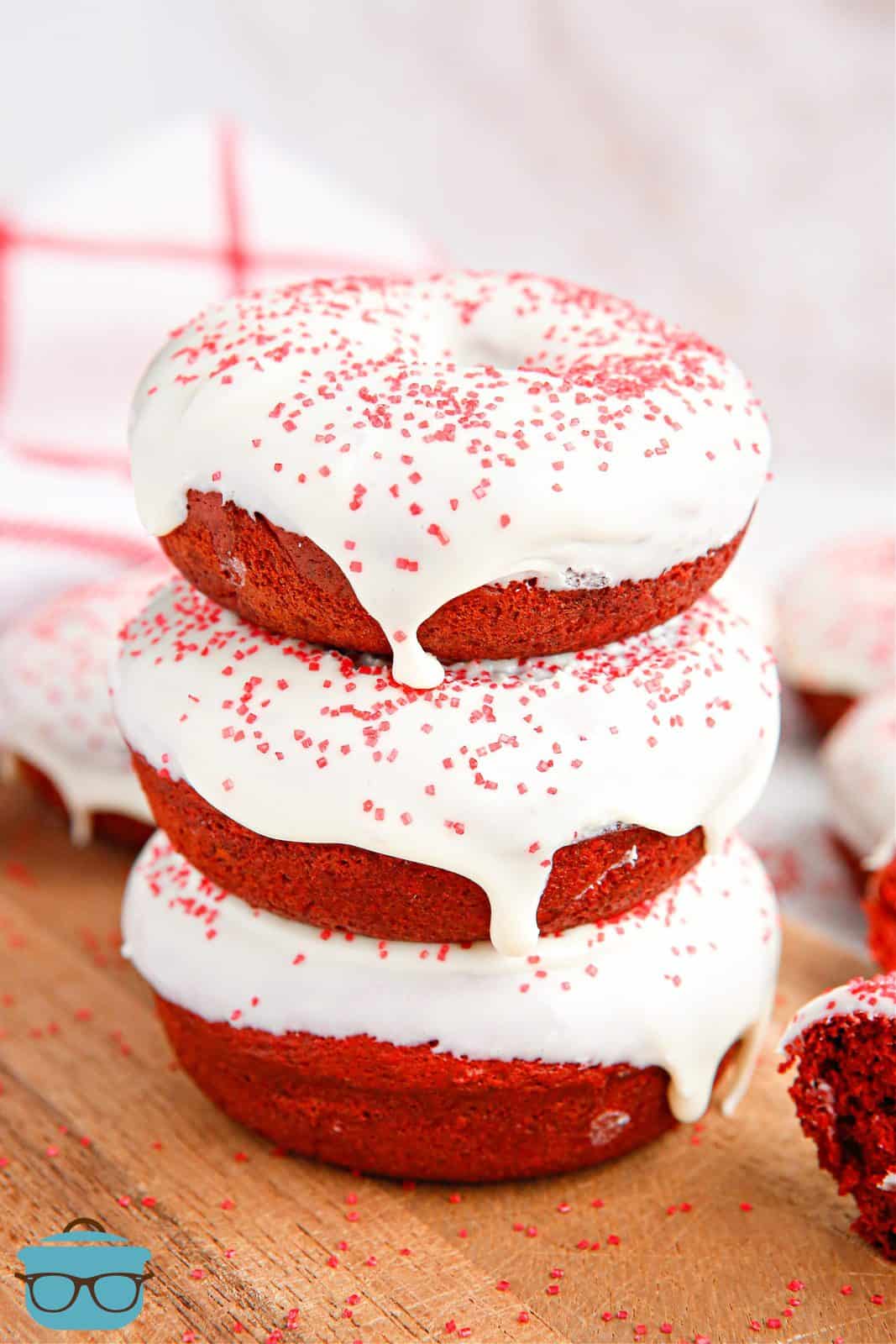 Three stacked and glazed Baked Red Velvet Donuts on cutting board.