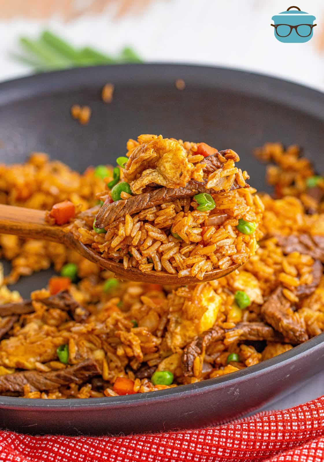 Wooden spoon holding up some of the Beef Fried Rice out of pan.