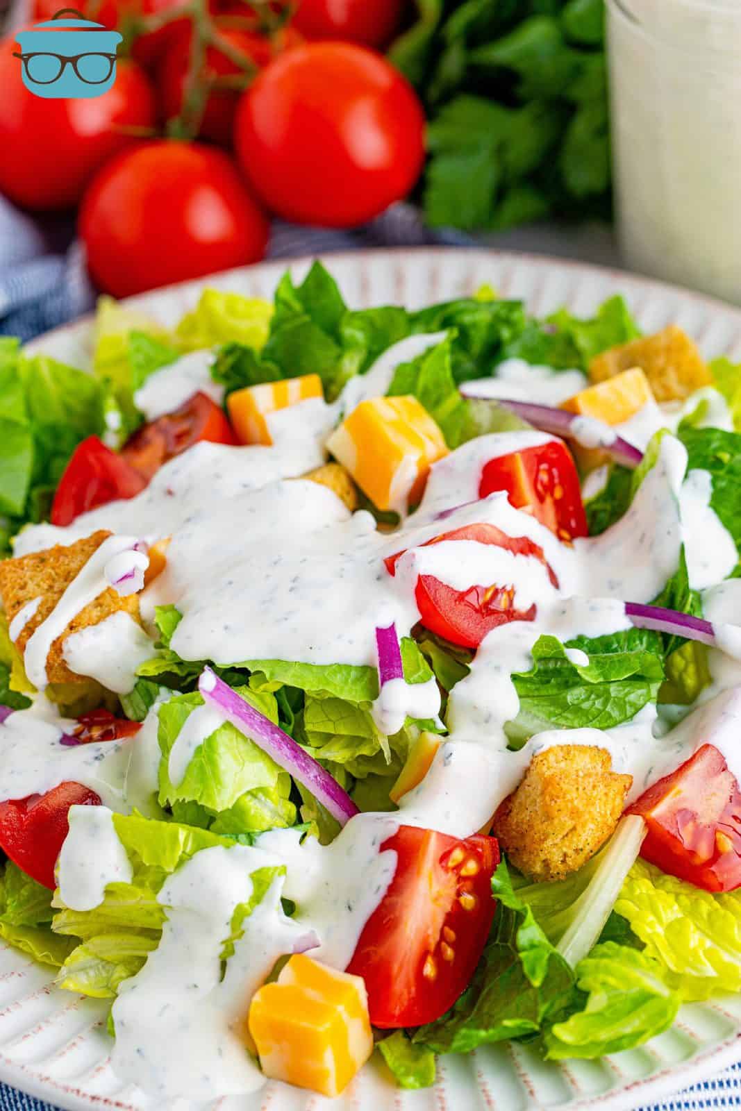 homemade ranch dressing shown poured onto a fresh green salad in a white bowl. 