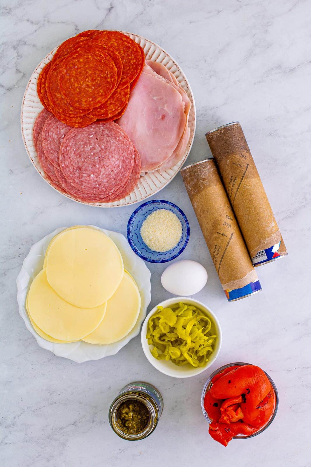 Ingredients needed: crescent roll dough sheets, provolone cheese, pepperoni, deli ham, genoa salami, roasted red bell peppers, pepperoncini’s, egg, pesto and parmesan cheese.