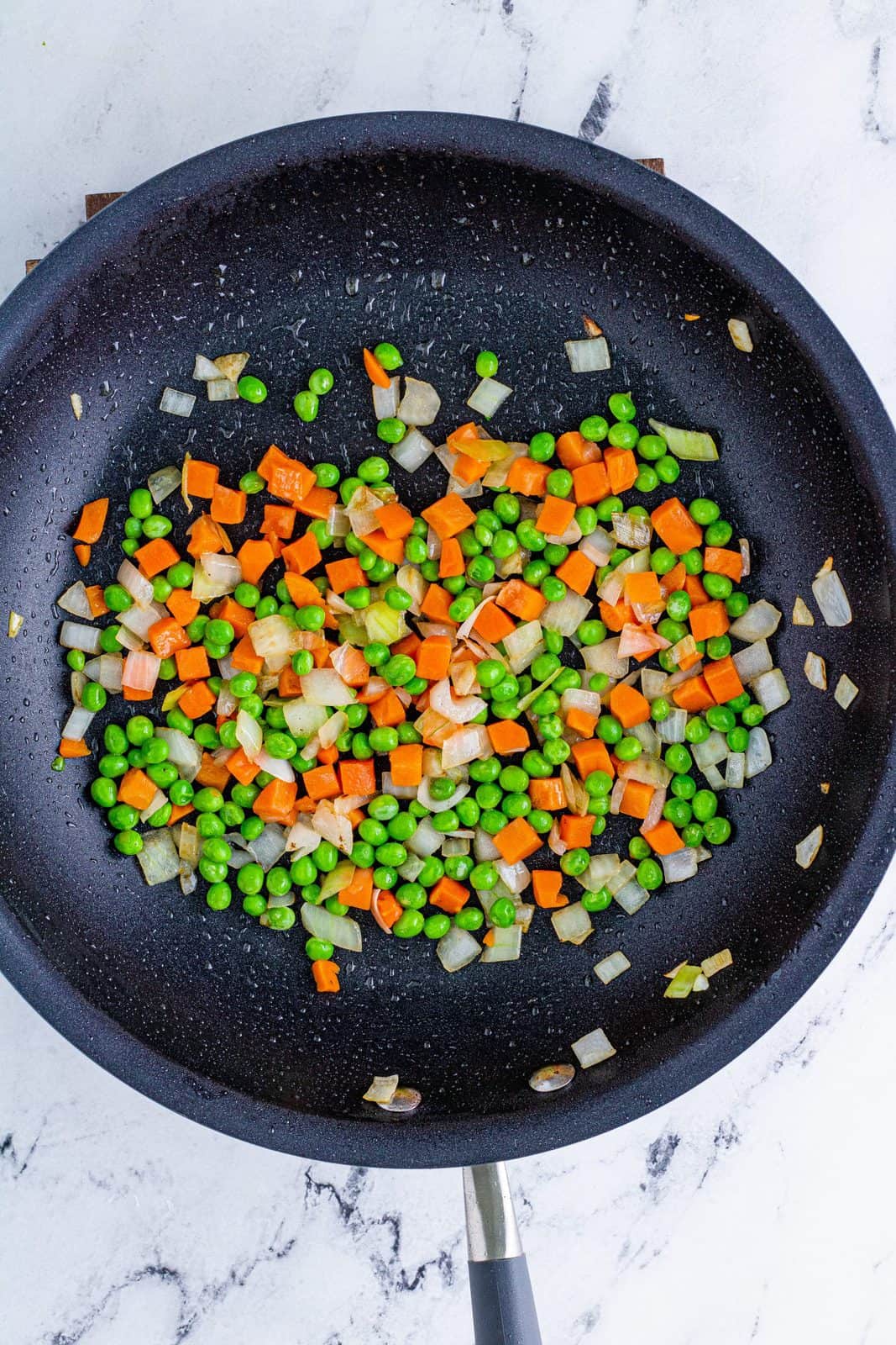 Onions, peas and carrots cooking in pan.
