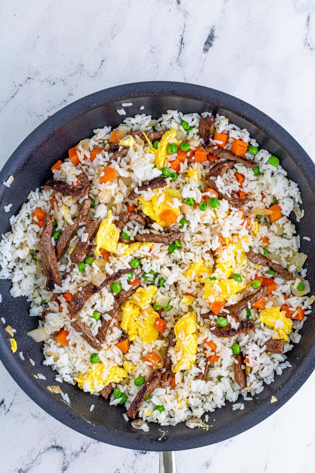 Beef, vegetables and eggs stirred into rice in pan.