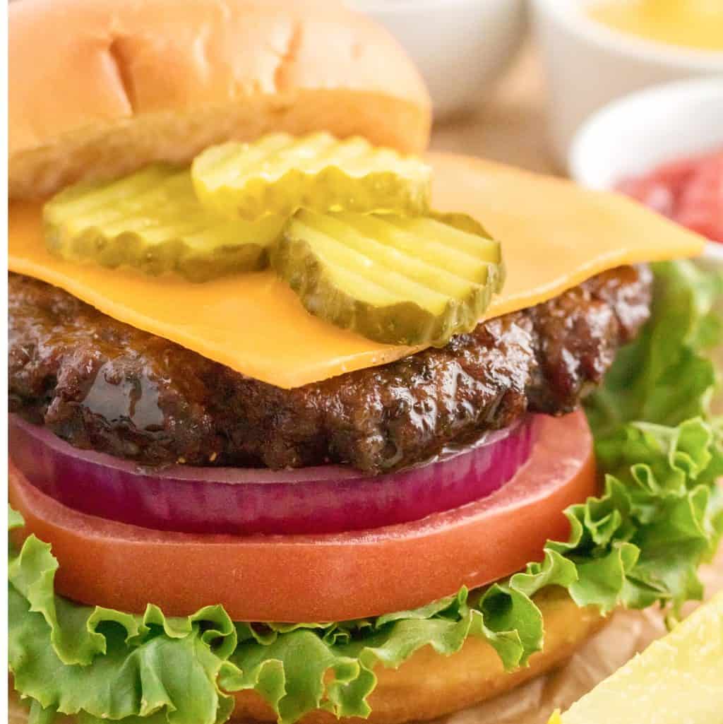 Square image close up of Air Fryer Hamburgers with toppings and bun off to the side.