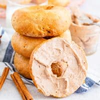 Square image of stacked Air Fryer Cinnamon Bagels with one cut in half spread with cinnamon honey butter.