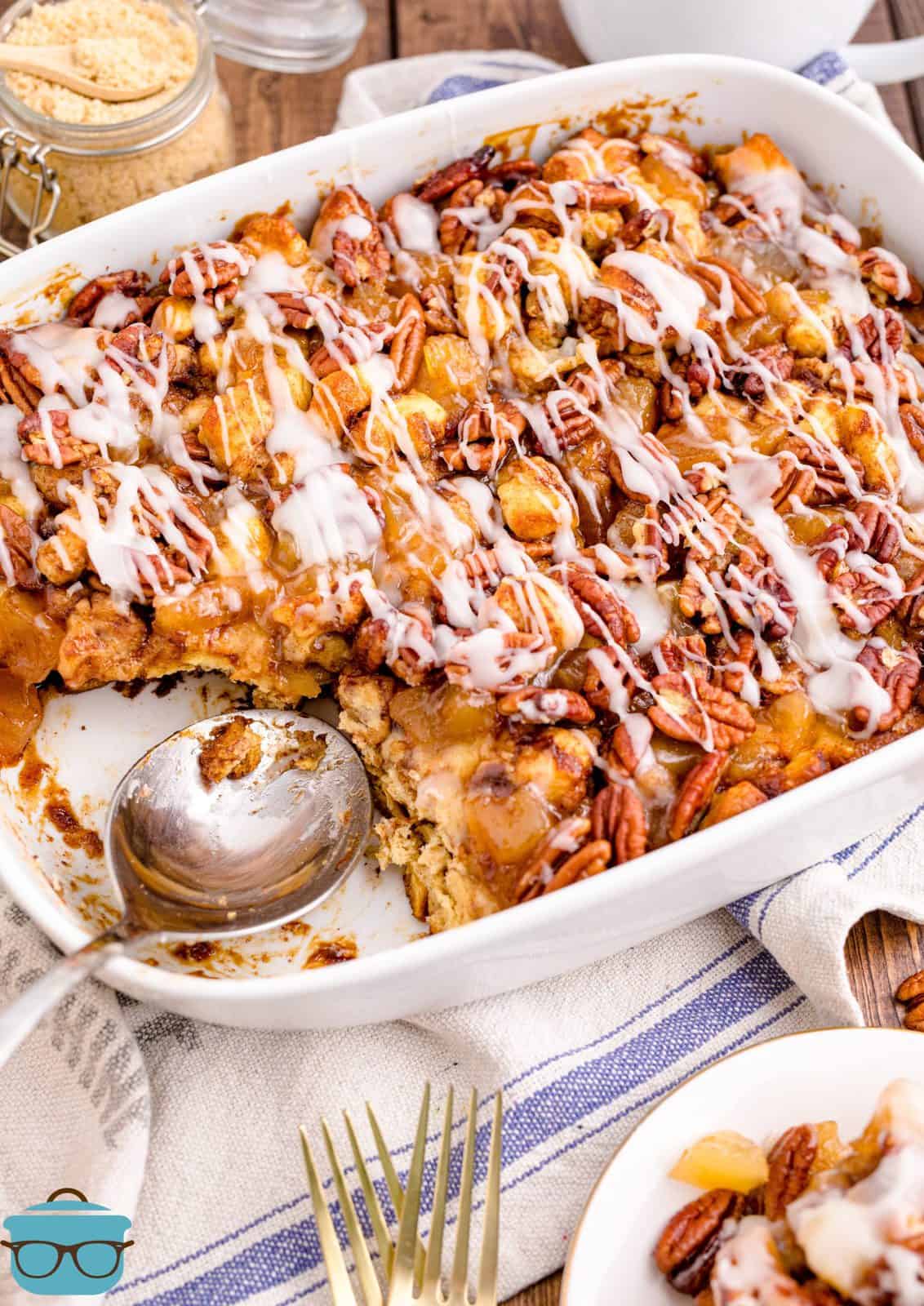 Cinnamon Roll Casserole in casserole dish with some missing with serving spoon in dish.