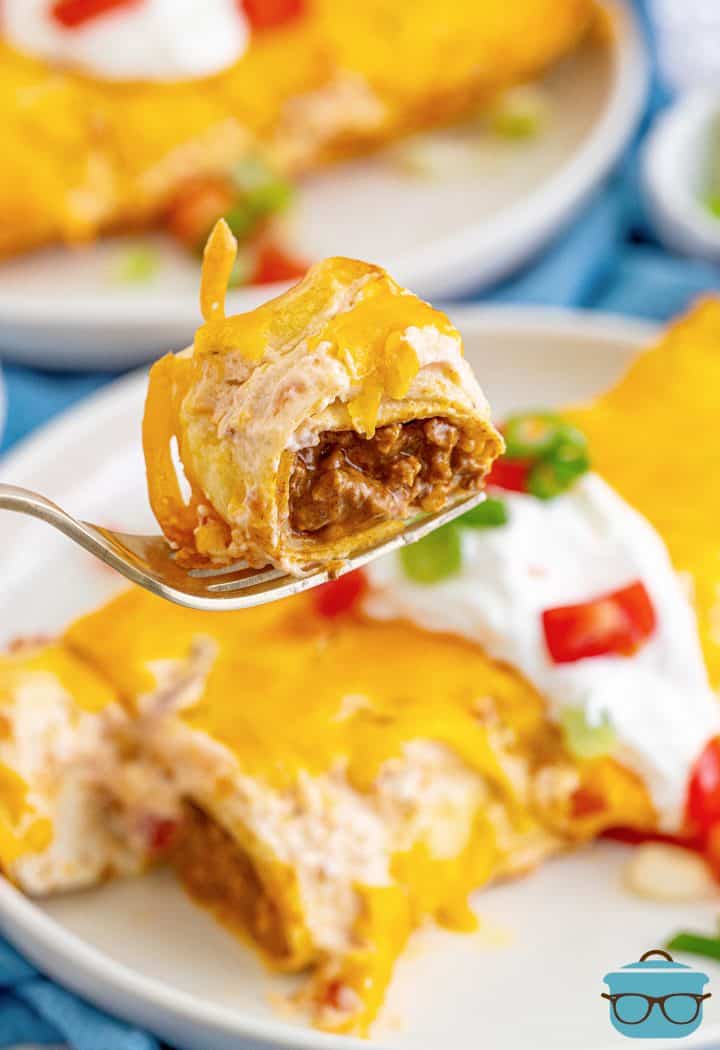 Fork holding up bite out of Ground Beef Enchiladas.