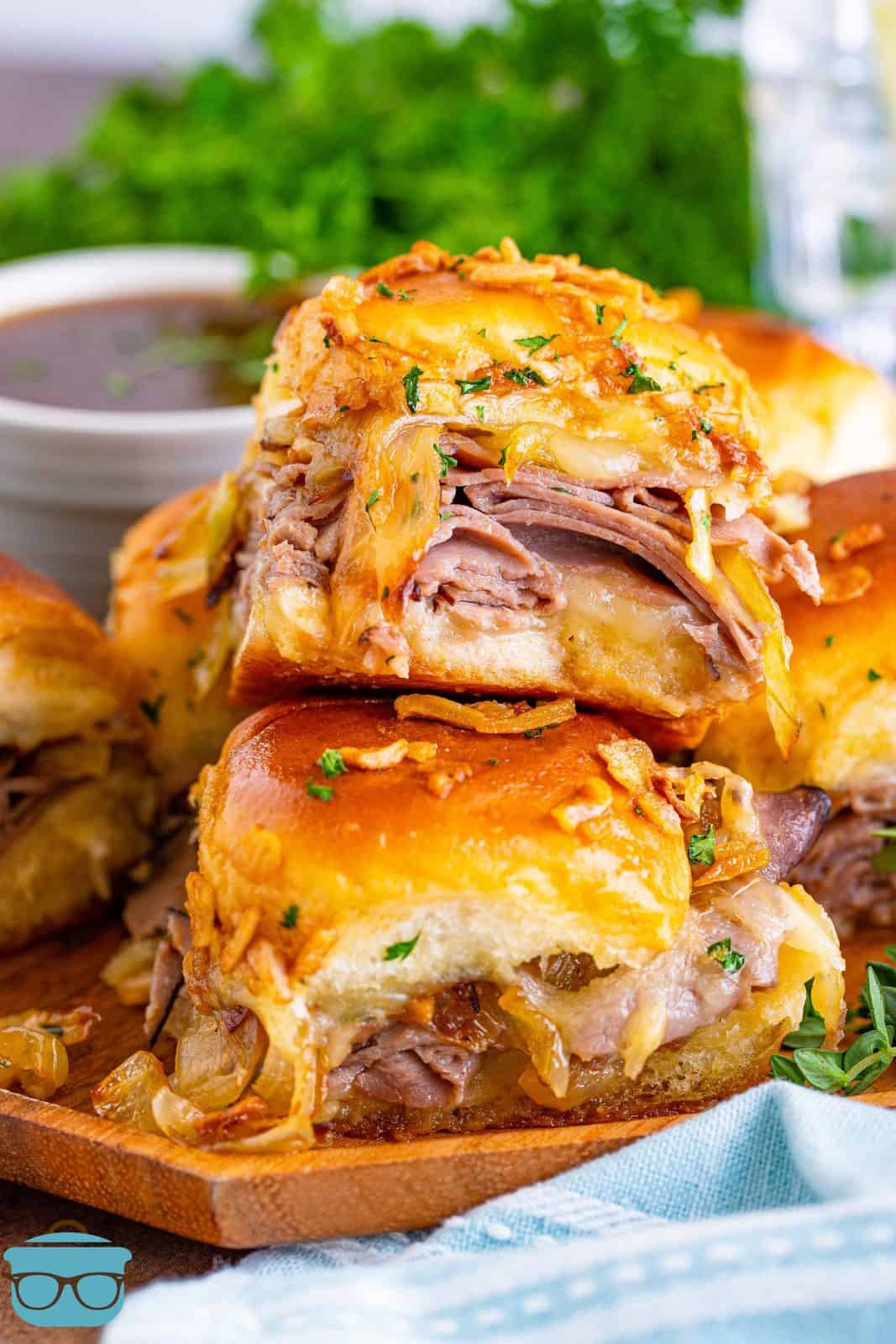Close up of stacked French Dip Sliders on plate with melted cheese and onions.