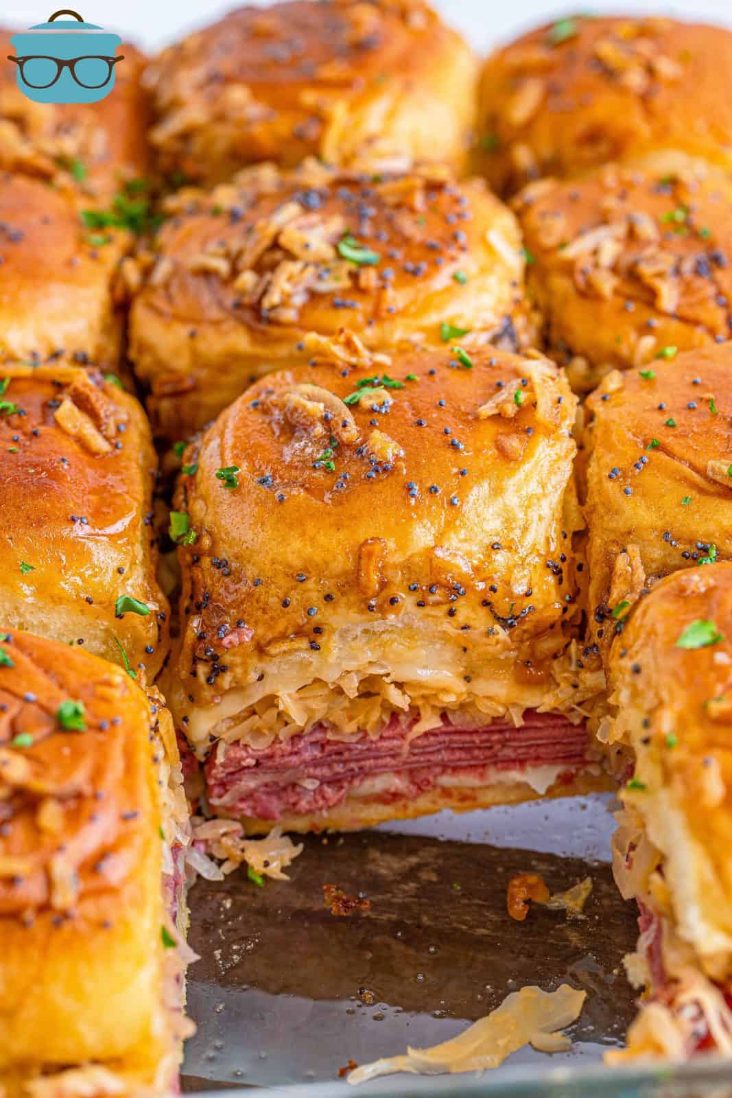 Reuben Sliders in baking pan with one taken out showing layers.