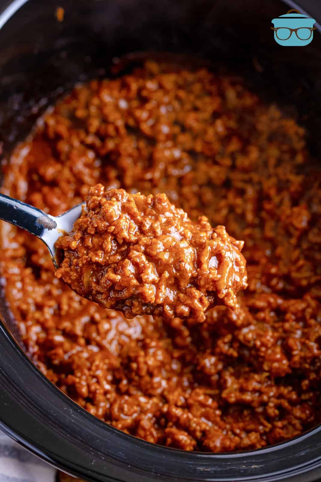 a large spoon scooping up some sloppy Joe mix over a slow cooker. 