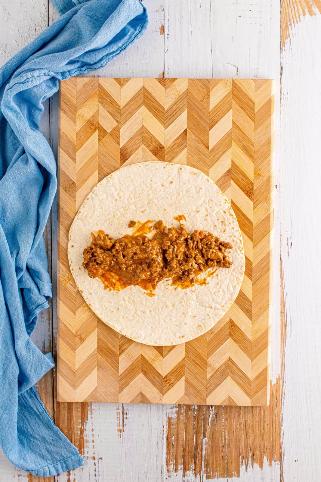 Ground beef mixture spread onto one tortilla on cutting board.