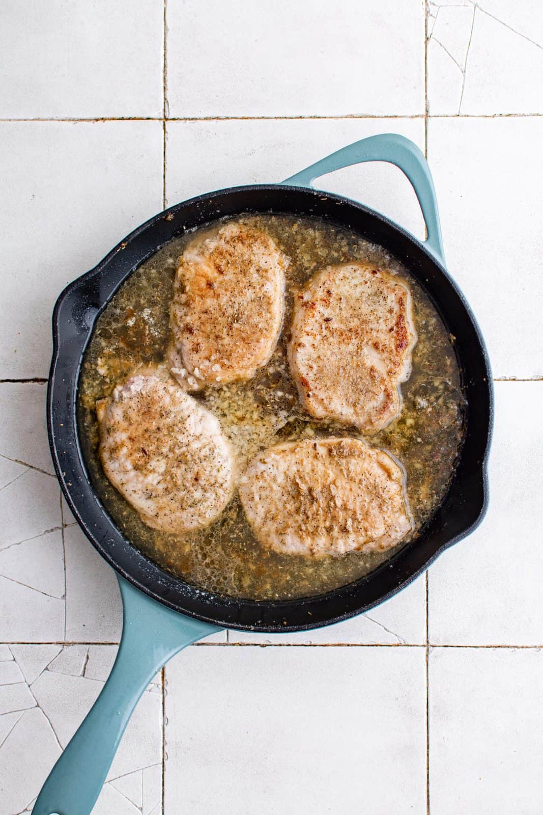 Sauce added to pork chops in pan.