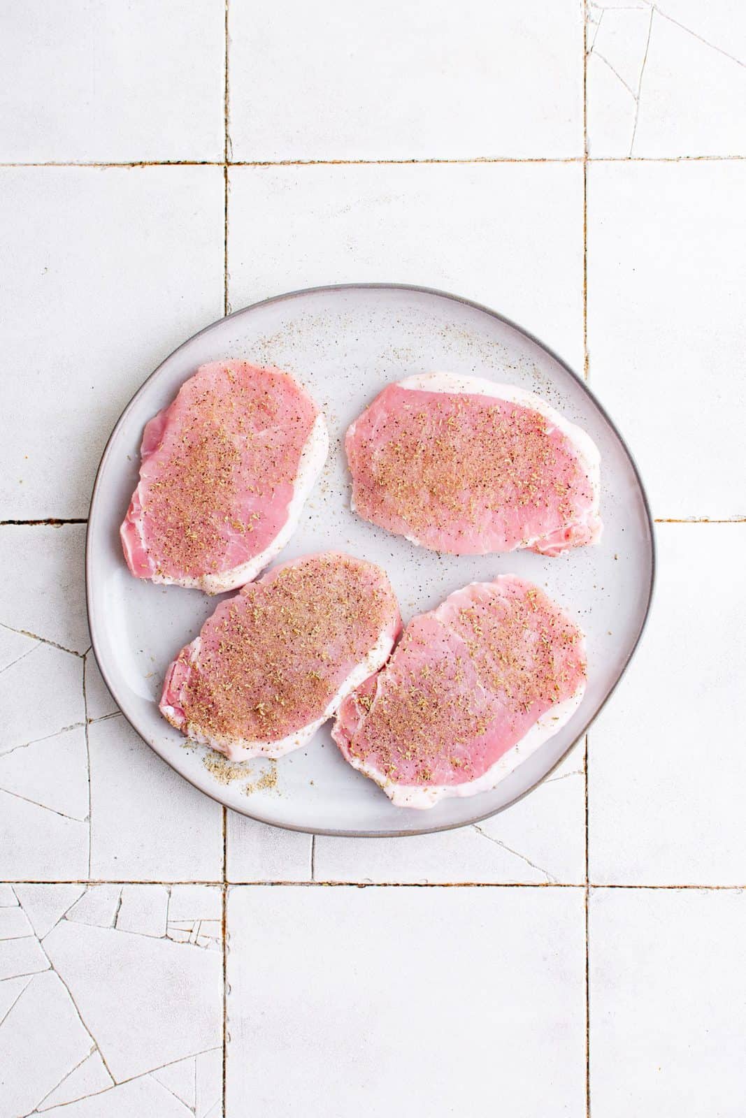 Pork chops on plate seasoned with seasonings.