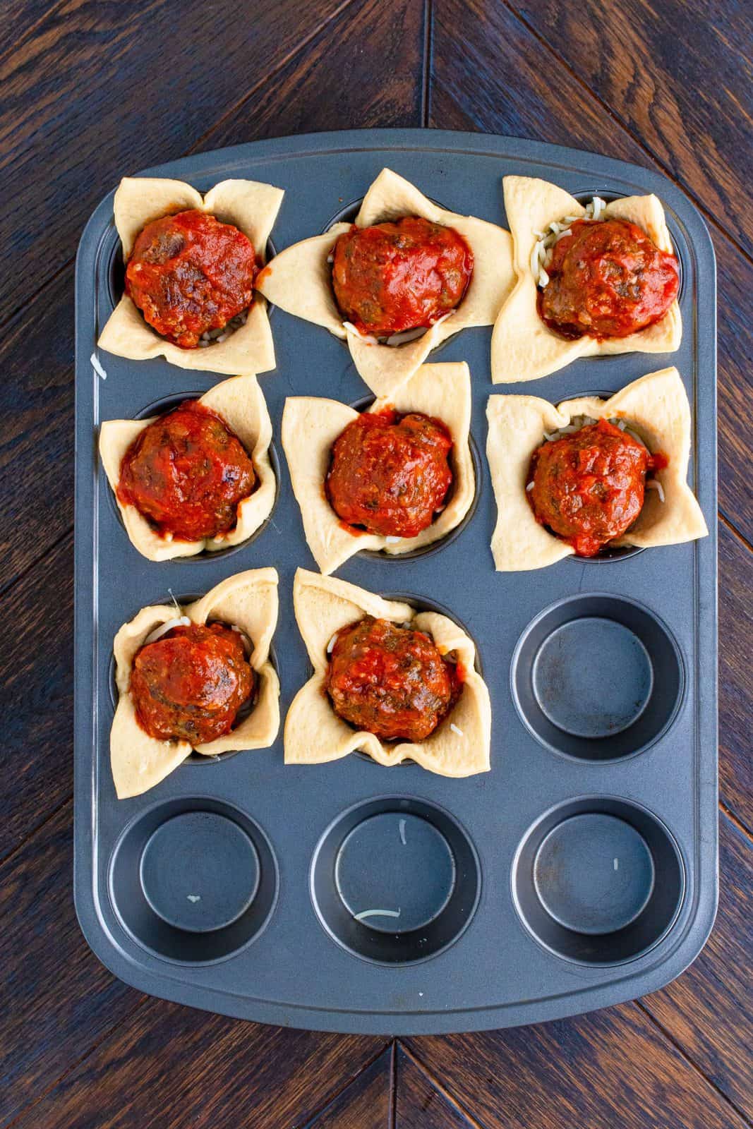 Meatballs added to top of cheese in muffin tin.