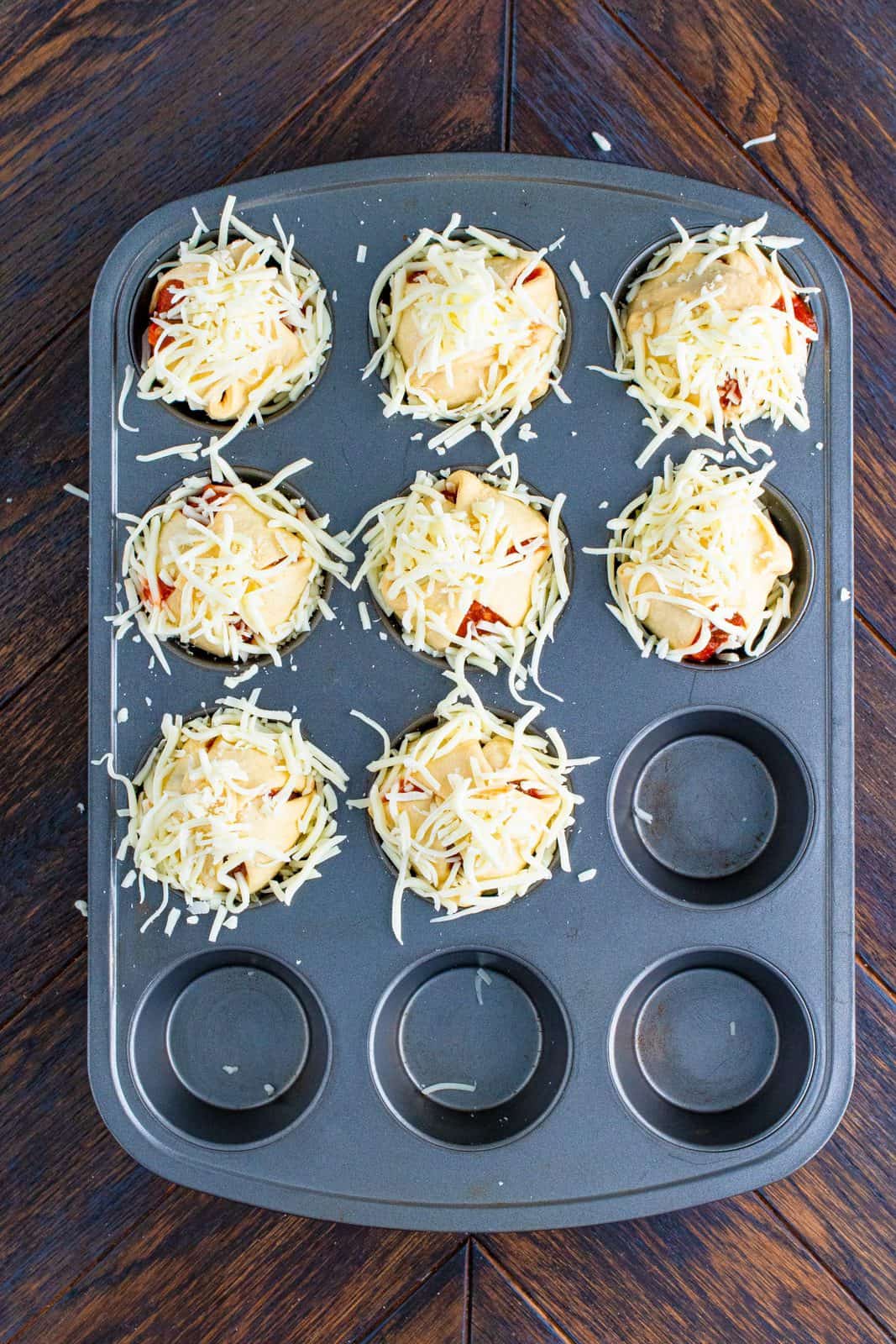 Cheese placed on top of folded crescent dough sheets in muffin tin.