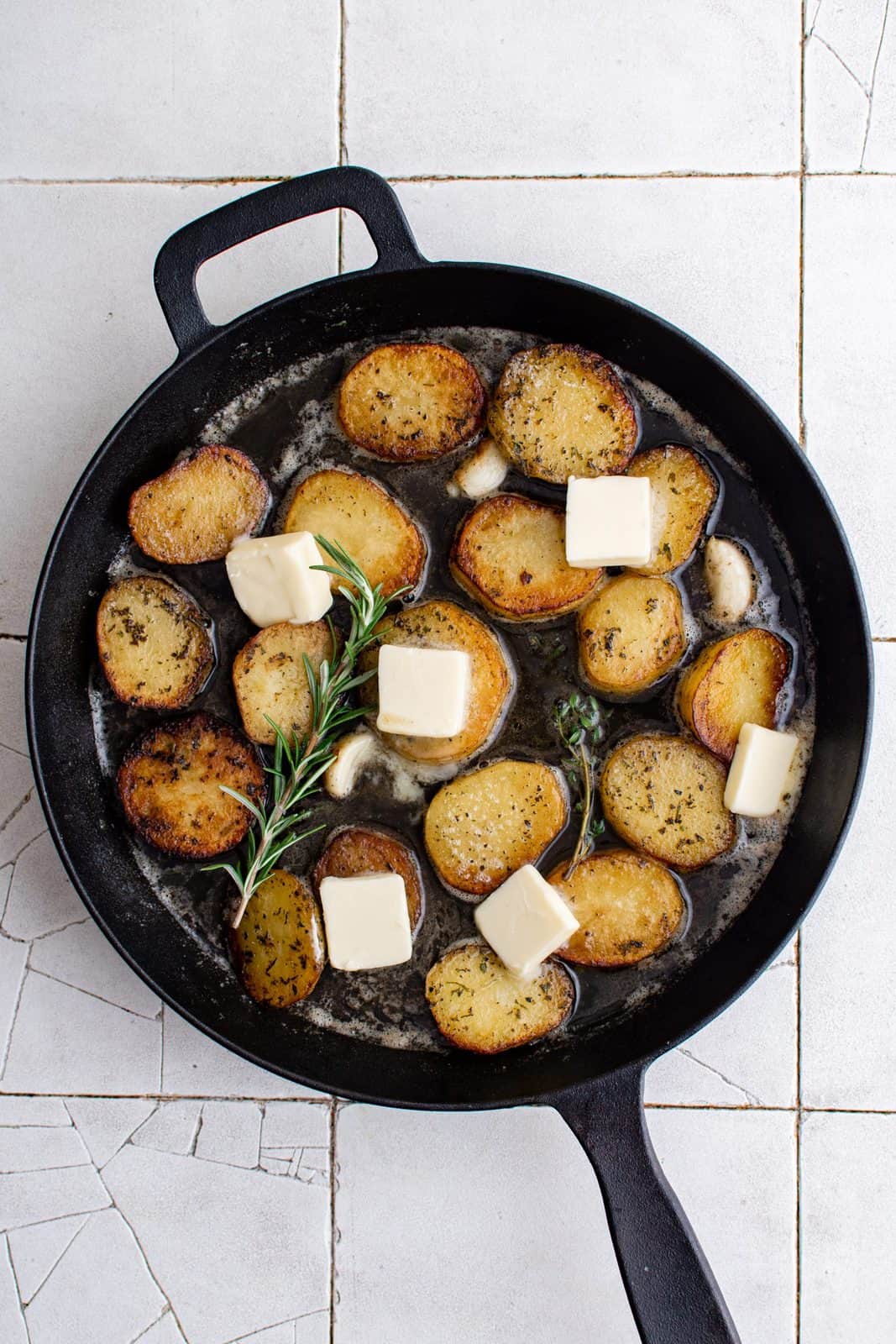 Slices of butter added to top of potatoes in pan.