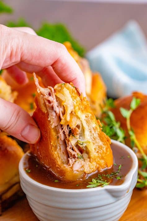 Hand dipping one French Dip Slider in Au Jus.