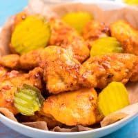 Square image of finished Air Fryer Nashville Hot Chicken Nuggets in bowl with pickles.