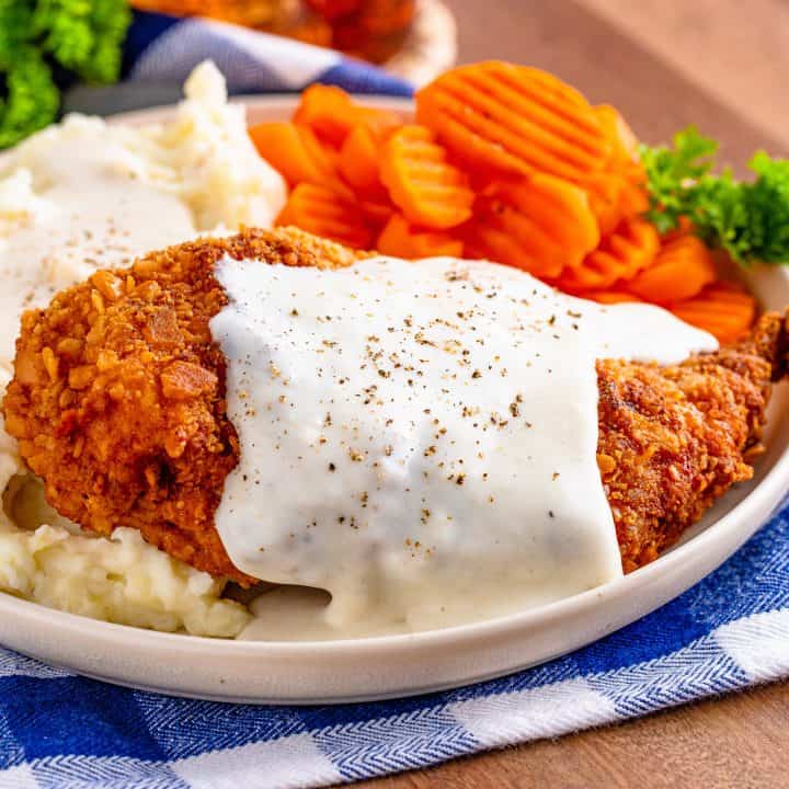 Square image of gravy poured over Chicken Fried Chicken on plate with sides.